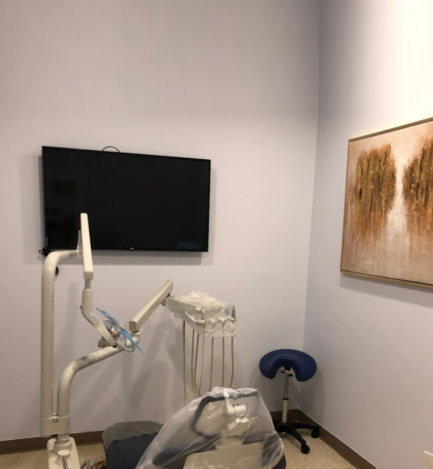 The image shows an interior space that appears to be a dental or medical office, with a large TV mounted on the wall displaying what looks like a digital screen, and various dental equipment including a dental chair and a dental mirror.