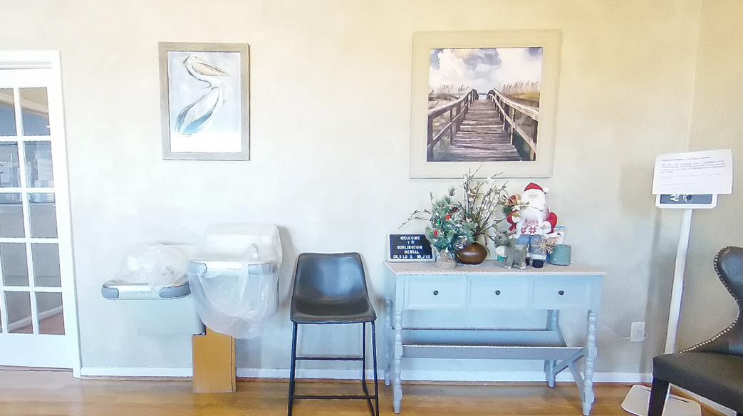 The image shows an interior space with a wall-mounted picture frame, a chair, a desk with a computer monitor and keyboard, and a room divider. There is also a potted plant on the floor.