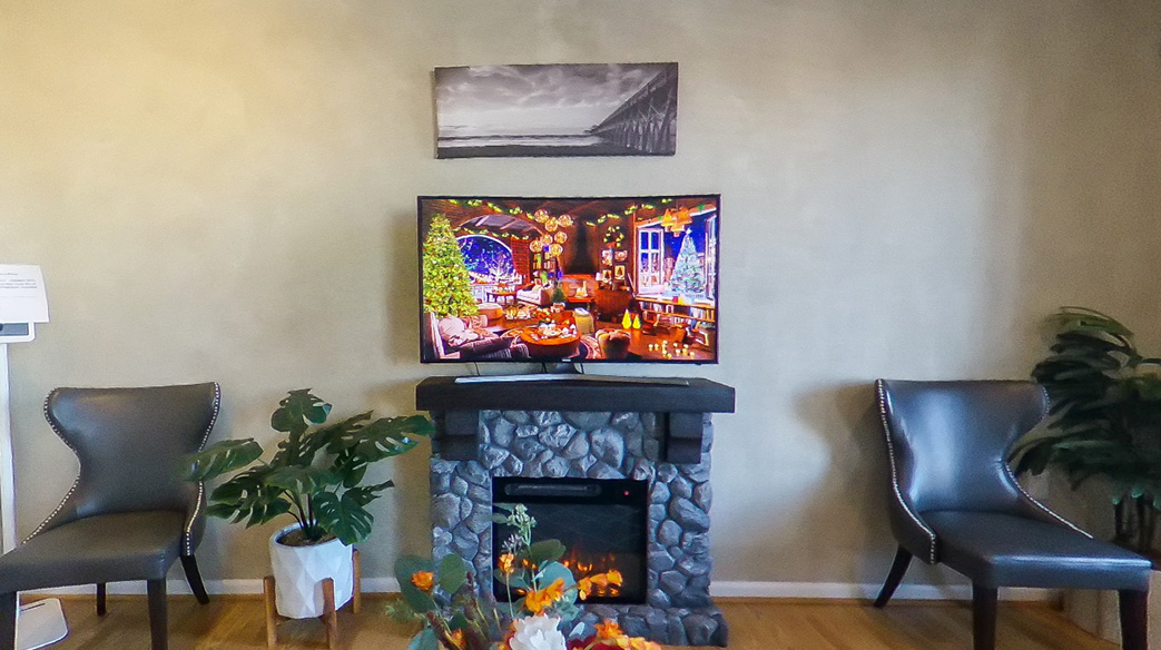A modern living room with a fireplace, a flat-screen TV displaying a colorful scene, and two chairs in front of the fireplace.