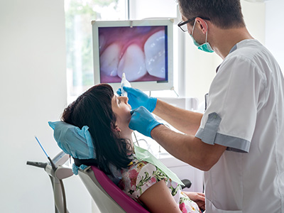 A dental professional performing a procedure on a patient in a clinical setting, with the patient seated in a chair and the professional standing.