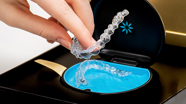 Hand holding a clear plastic tray containing blue toothpaste and a white electric toothbrush.