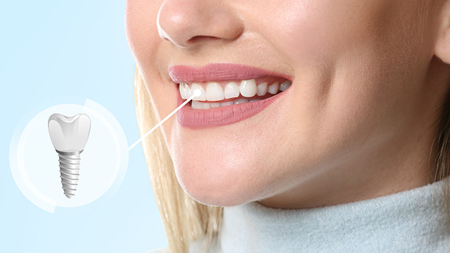 A woman with a toothbrush in her mouth, smiling at the camera.
