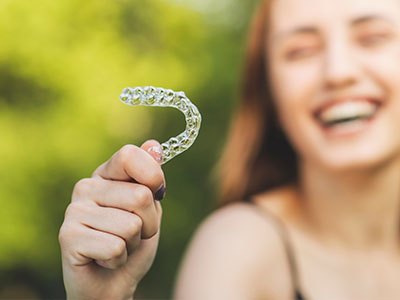 A smiling woman holding a clear, plastic toothbrush with bristles.