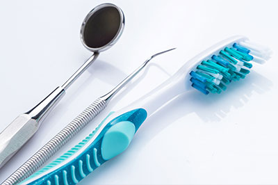 The image displays a collection of dental care items, including a toothbrush with blue bristles, a pair of tweezers, and a small spoon-like instrument, all set against a white background.