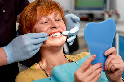 The image shows a woman in a dental chair receiving oral care, with a dental professional adjusting her teeth using tools and a blue mouthguard.