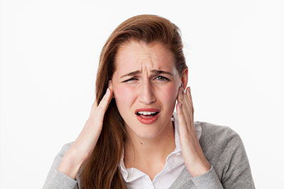 A woman with her hand on her head, possibly in pain or confusion, against a white background.