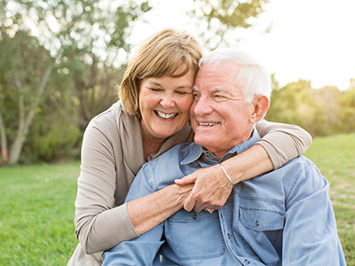 An elderly couple embracing each other outdoors in daylight.