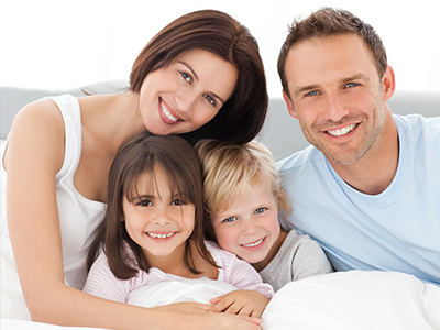 A family of five, including a man and woman, posing together in bed with smiles.