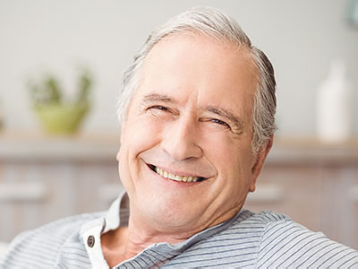 An elderly man with white hair and a smile, sitting in an armchair.