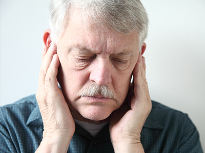 An older man with a mustache, holding his hand to his ear in a pained or disoriented expression.